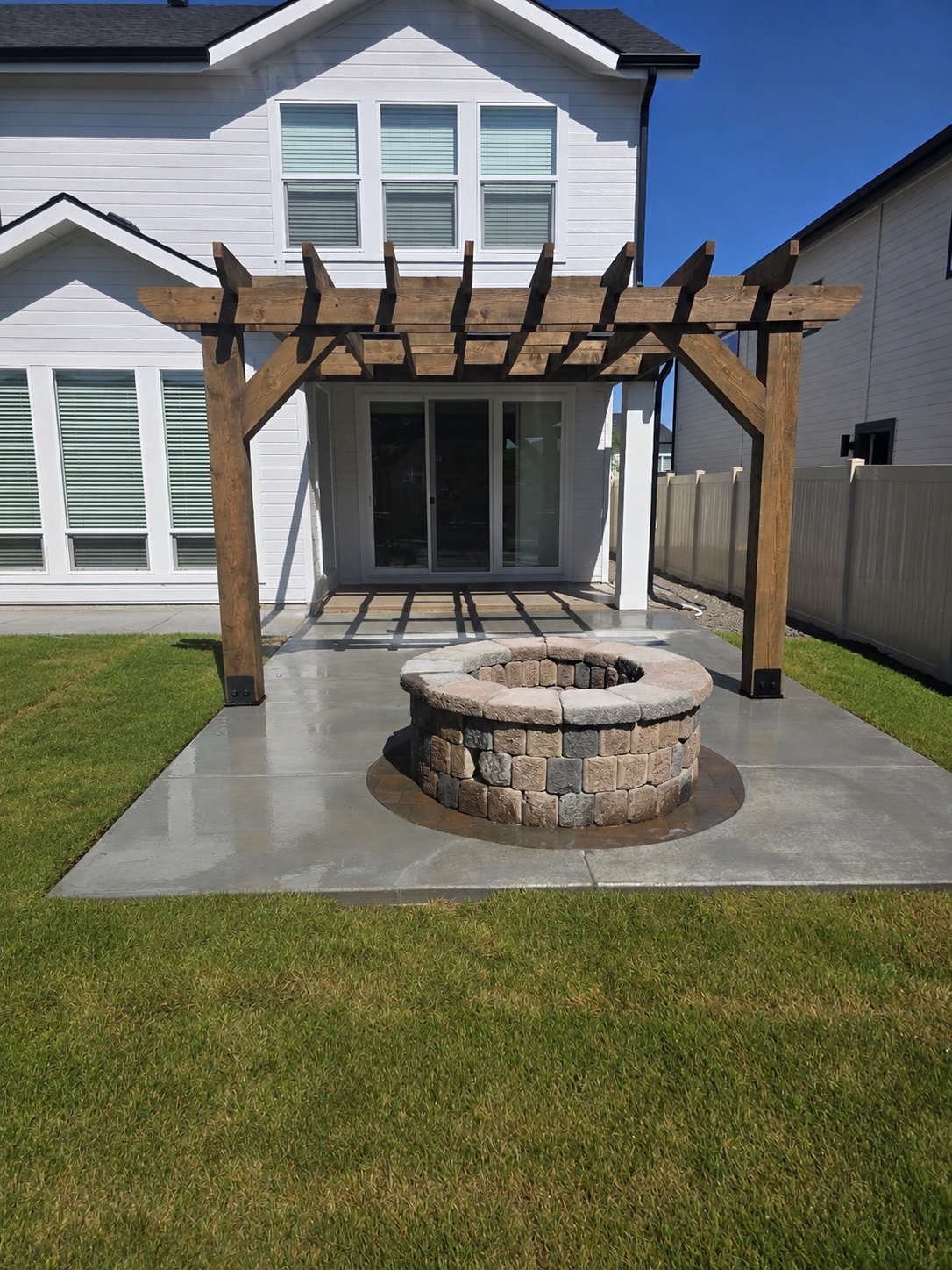 Finished stone fire pit on a concrete patio beneath a timber pergola