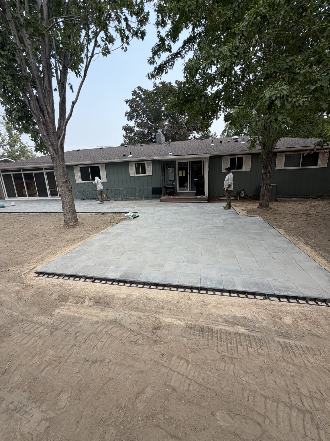 Wide view of a rectangular gray paver patio extending from a Boise home's back door beneath mature trees